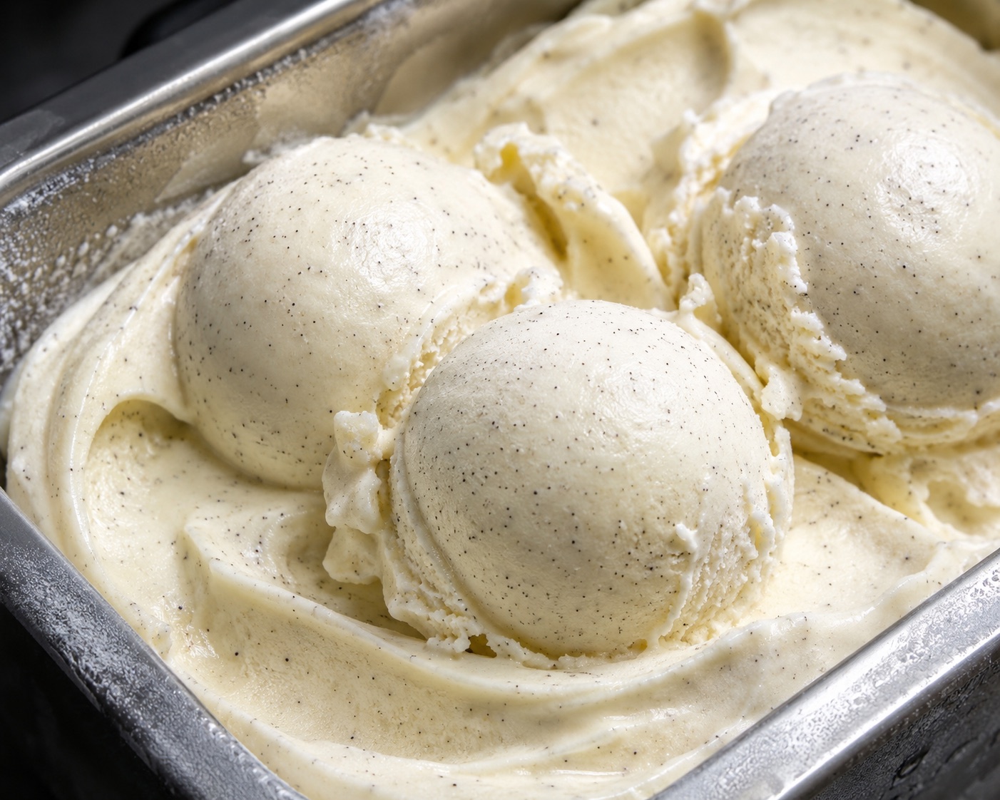 Scoops of homemade vanilla bean gelato with visible vanilla seeds in a chilled metal pan